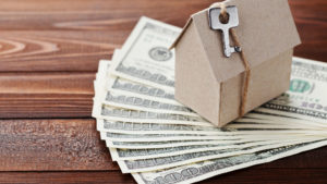 cardboard house with key tied on sitting on top of money